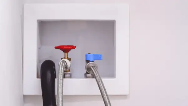 Washing machine installation: water inlet valves with hoses attached, ready for hookup.