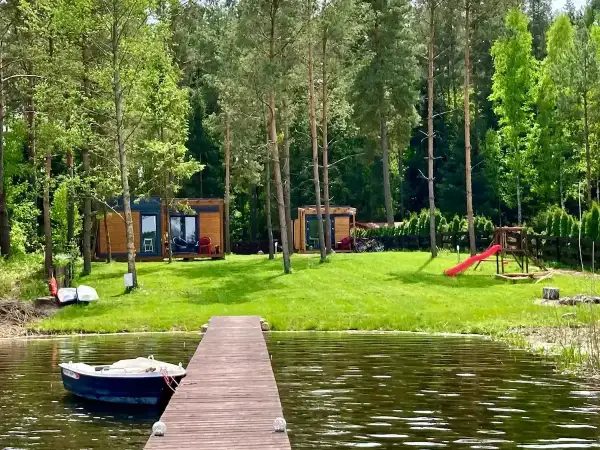 Idealne miejsce na wakacje w Polsce: drewniane domki, jezioro z łódką i plac zabaw dla dzieci.