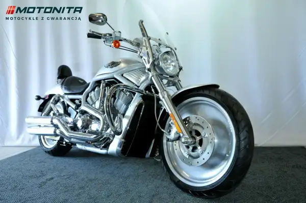 Srebrny motocykl typu cruiser z chromowanymi elementami, na tle białej ściany.