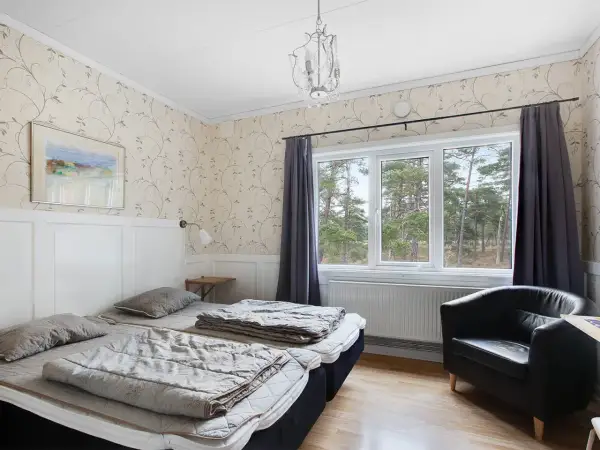 Mysigt rum på vandrarhem Gotland med två sängar, fåtölj och fönster med utsikt över skog.