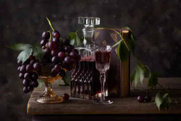 Kieliszek wina merlot veneto obok karafki i kiści winogron na drewnianym stole.