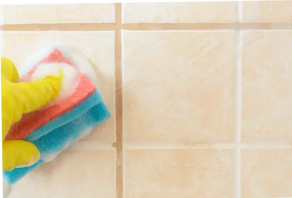 Mano con guanto giallo che pulisce le piastrelle del bagno con una spugna bagnata di schiuma.