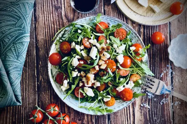 Frischer Rucola Salat mit Kirschtomaten, Feta und Croutons auf rustikalem Holztisch.