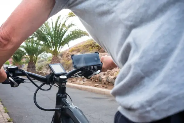 Persoon op een speed pedelec, die een motorvoertuig is, met telefoonhouder en display. Palmbomen op de achtergrond.