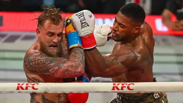 Two boxers grapple in the ring. One, with tattoos and wet hair, recoils from a punch. The other, muscular and focused, lands a blow. This is what heavyweight boxing looks like.