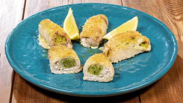 Involtini di pesce spada ripieni di erbe aromatiche, dorati e serviti su un piatto blu con spicchi di limone.