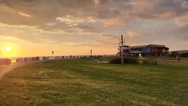Sonnenuntergang am Husum Strand mit Strandkörben, einem Spielplatz und einem bunten Gebäude.