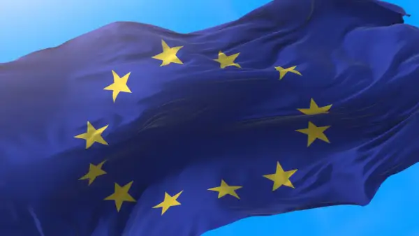 Flaga Unii Europejskiej falująca na wietrze na tle błękitnego nieba.