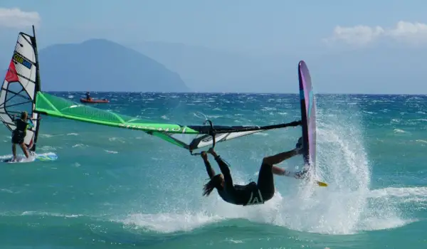 Windsurfer wykonuje akrobację na turkusowej wodzie, tworząc fontannę rozprysków.