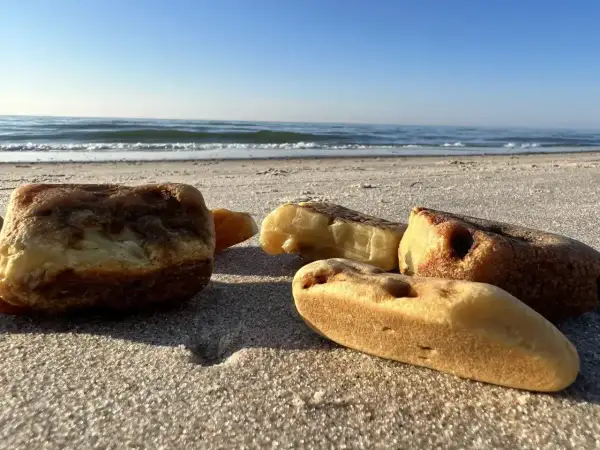 Kilka kawałków bursztynu leży na piaszczystej plaży, z morzem i błękitnym niebem w tle.