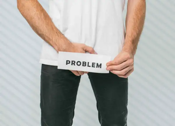 Mężczyzna trzyma kartkę z napisem "PROBLEM" w okolicy krocza.