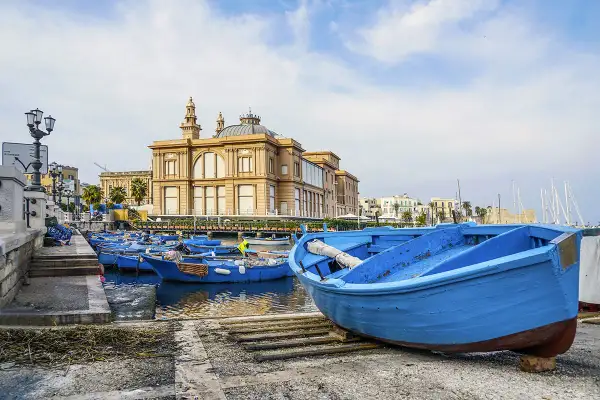 Barche blu nel porto del capoluogo della Puglia, con un edificio storico sullo sfondo.