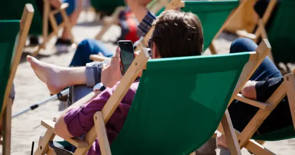 Mężczyzna w okularach przeciwsłonecznych relaksuje się na leżaku, przeglądając telefon. Idealny urlop wypoczynkowy.