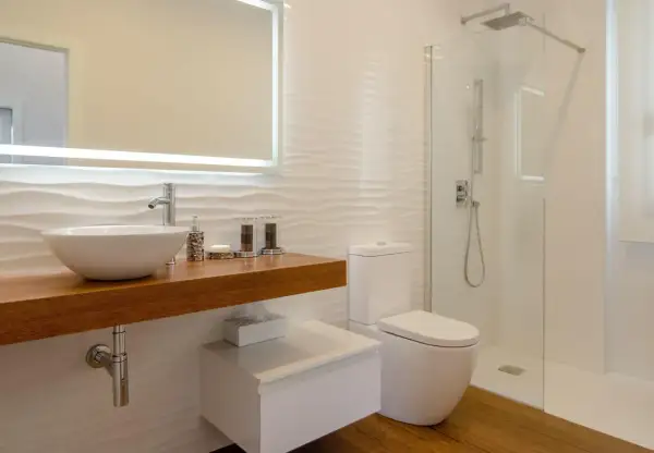 Baño moderno con lavabo sobre mueble de madera, inodoro y ducha con mampara de cristal. Perfecto para impermeabilizar ducha y mantener la limpieza.