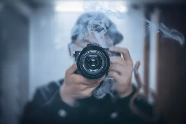 Osoba w kapturze śledzi i fotografuje gwiazdy przez obiektyw aparatu, otoczona mgiełką dymu.