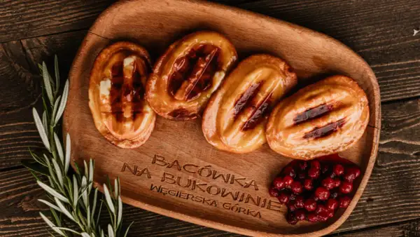 Cztery grillowane oscypki z żurawiną i rozmarynem na drewnianej desce.