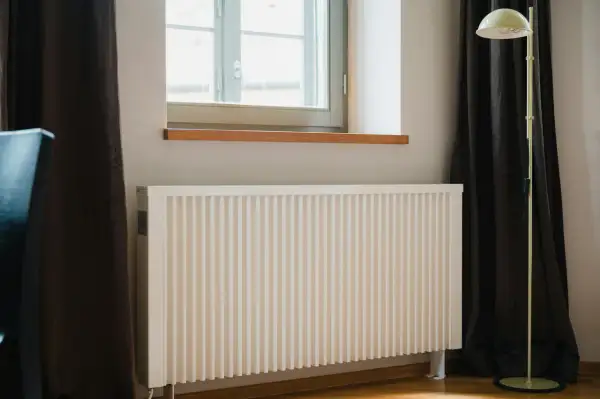 Vitt element med ribbad front, perfekt för att bygga elementskydd. En golvlampa står bredvid.
