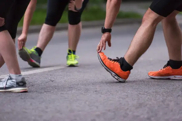Atleti si preparano per la gara di corsa, allungando le gambe e indossando scarpe sportive colorate.