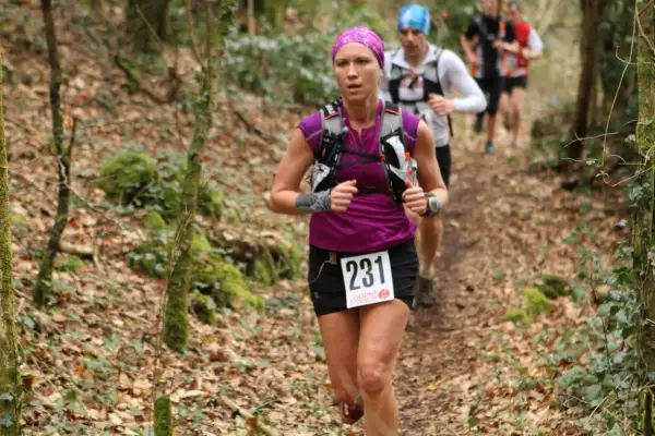 Une coureuse, dossard 231, s'élance sur un trail débutant en forêt. D'autres coureurs la suivent.
