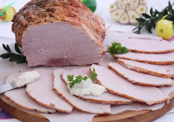 Pyszna szynka pieczona na obiad, pokrojona w plastry, podana z chrzanem i ziołami. Idealna na rodzinny posiłek.