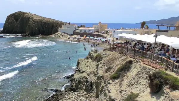 Gente disfrutando en un restaurante de Cabo de Gata, con vistas a una playa concurrida y el mar azul.