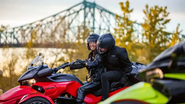 Para jadąca na czerwonym Can-Am Spyder, w tle most i jesienne drzewa.