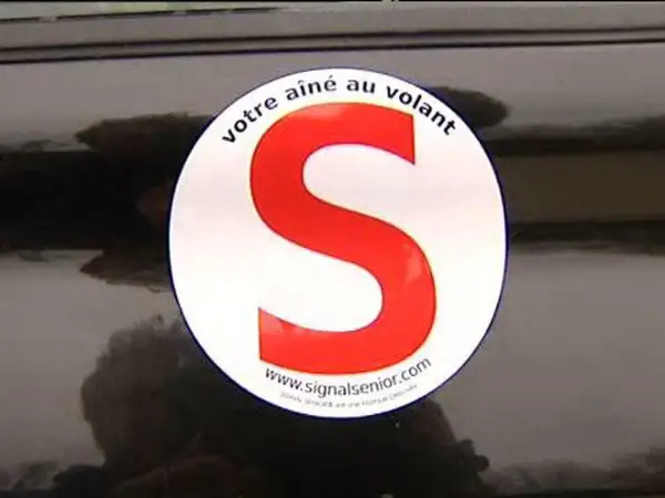 Macaron "votre aîné au volant" sur une voiture. Le S rouge est bien visible.