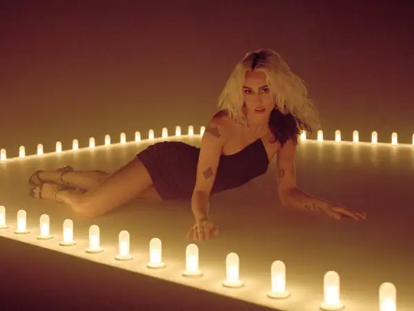 Miley Cyrus w stylizacji na "endless summer vacation" leży wśród rozświetlonych lamp.