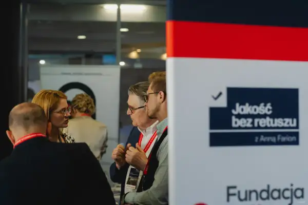 Ludzie rozmawiający na tle banera z napisem "Jakość bez retuszu".