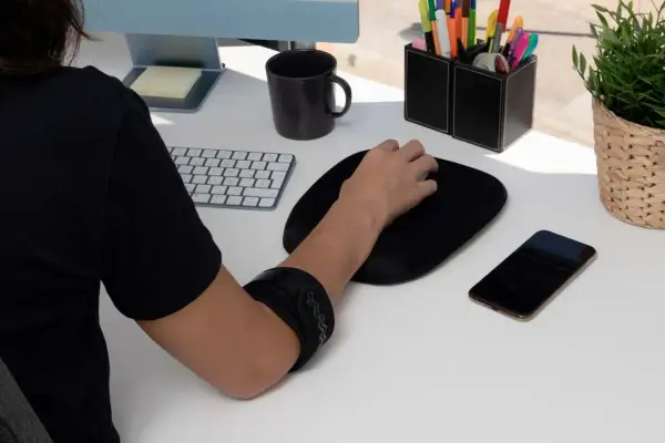Braccio con tutore per alleviare il dolore mano mouse. Tastiera, mouse, telefono e pianta sul tavolo.