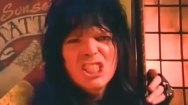 Rockman z lat 80. z burzą czarnych włosów i wykrzywioną twarzą, jakby śpiewał głośno utwory lat 80.