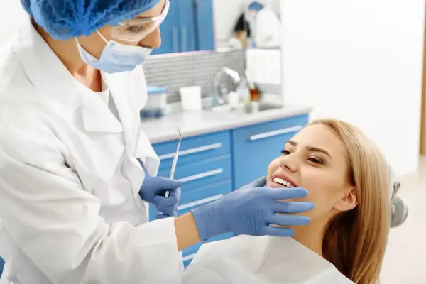 Dentystka bada uśmiechniętą pacjentkę, by wykluczyć zapalenie okostnej i ropień zęba.