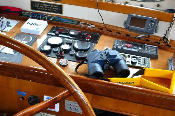 Un binocolo da ingrandimento, pronto per scrutare l'orizzonte, riposa sul cruscotto di una barca, accanto a strumenti di navigazione e a un timone in legno lucido.