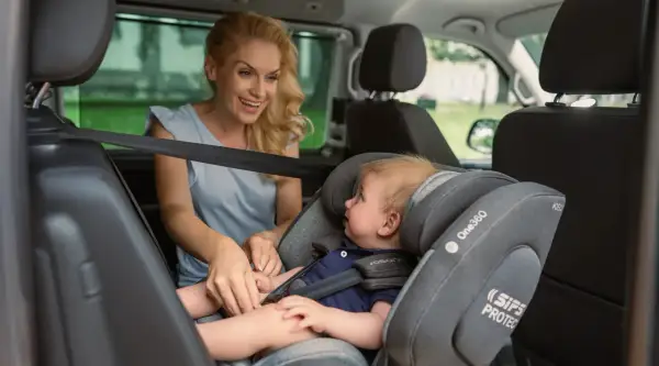 Lächelnde Mutter sichert ihr Baby im Kindersitz vorne im Auto.