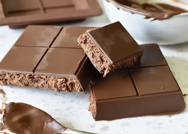 En fransk chokladtårta med krispigt fyllning, uppdelad i bitar. En sked med chokladkräm syns i förgrunden.