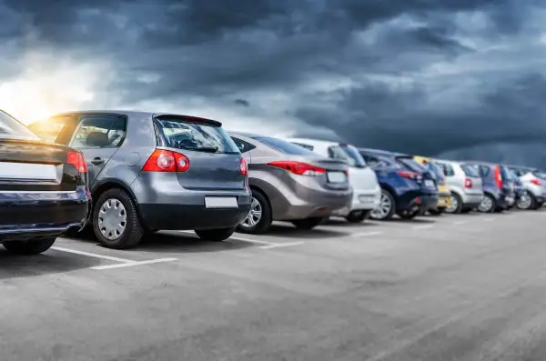 Rząd samochodów na parkingu, w tym jeden z włoską rejestracją, pod burzowym niebem.
