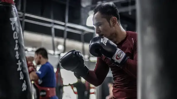 A boxer, sweating and focused, throws a powerful southpaw jab at a heavy bag in a dimly lit gym.