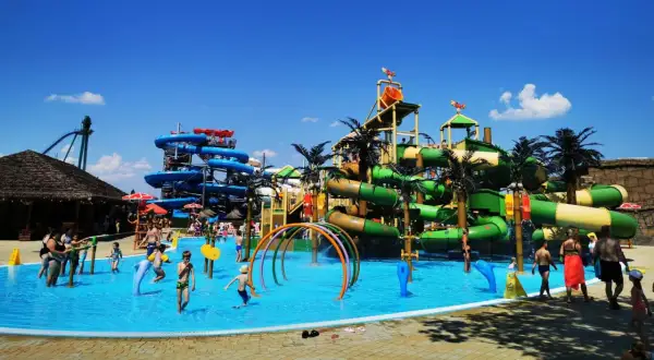 Wesoły wodny park rozrywki z mnóstwem zjeżdżalni, basenów i palm. Dzieci bawią się w wodzie, ciesząc się letnim dniem.