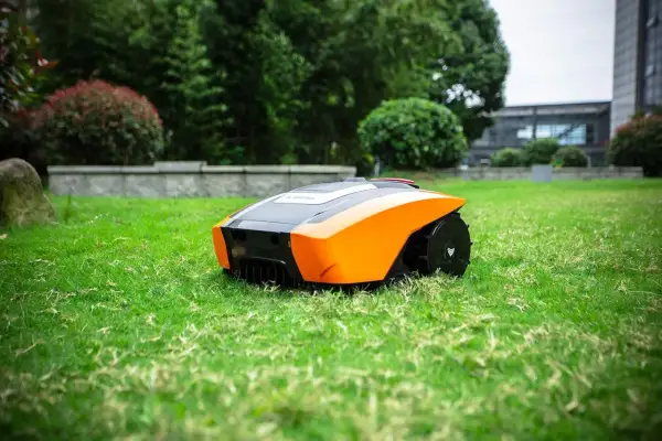Robot cortacésped autónomo de color naranja y negro, listo para mantener impecable el césped artificial de un jardín moderno.