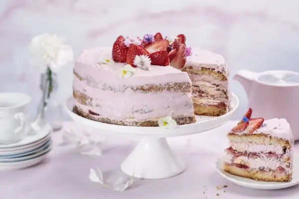 En vacker jordgubbstårta med rosa frosting, dekorerad med färska jordgubbar och blommor. Perfekt för ett somrigt fika, kanske inspirerad av ett enkelt jordgubbstårta recept.