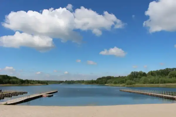 Piękny, słoneczny dzień nad jeziorem Wilczyńskim. Piaszczysta plaża, drewniane pomosty i błękitne niebo z białymi chmurami zapraszają do wypoczynku.
