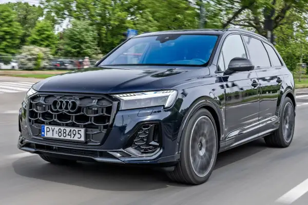 Ciemny Audi Q7 w ruchu ulicznym, z grillem i światłami LED. Sprawdź audi q7 cena i możliwości tego luksusowego SUV-a.