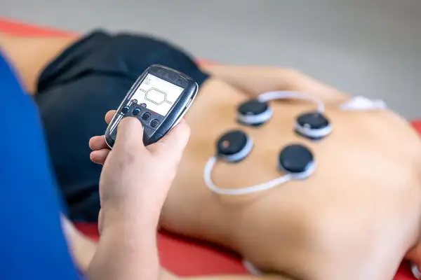 Osoba z pilotem steruje elektrodami na plecach. Trening EMS może przynieść korzyści, ale warto znać potencjalne trening ems skutki uboczne.