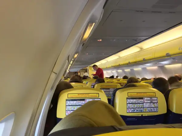 Wnętrze samolotu Ryanair, pasażerowie siedzą w rzędach. Na oparciach siedzeń widoczne są żółte tabliczki z instrukcjami bezpieczeństwa, co może uspokoić osoby zastanawiające się, czy Ryanair jest bezpieczny.