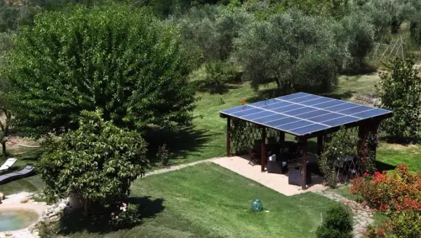 Un pergolato con pannelli fotovoltaici a terra in giardino, in linea con la normativa, offre ombra e energia pulita.