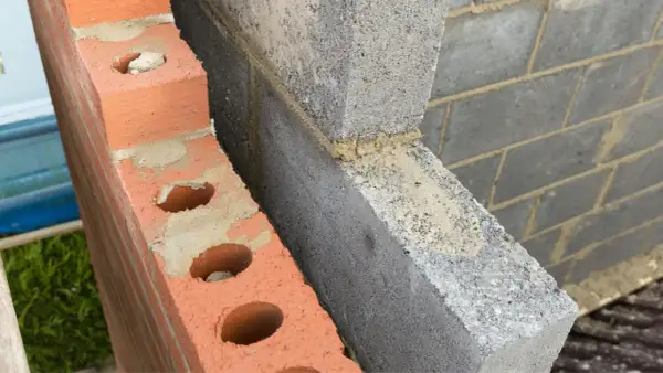 Dettaglio di una parete in costruzione con mattoni rossi forati e blocchi di cemento grigio. Si intravede lo spazio vuoto tra le due murature, ideale per l'**insufflaggio pareti**.