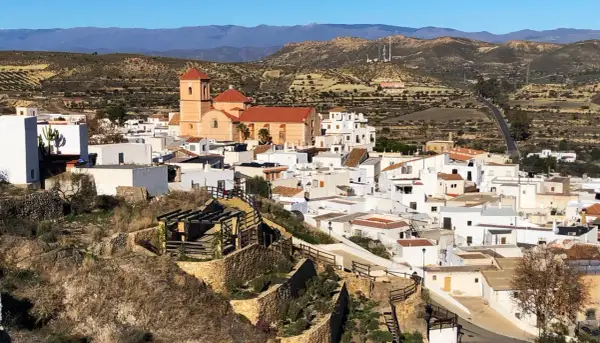Vista panorámica de Lucainena de las Torres, un pueblo blanco andaluz con una iglesia de tejado naranja y montañas al fondo. ¡Un lugar con mucho que ver!