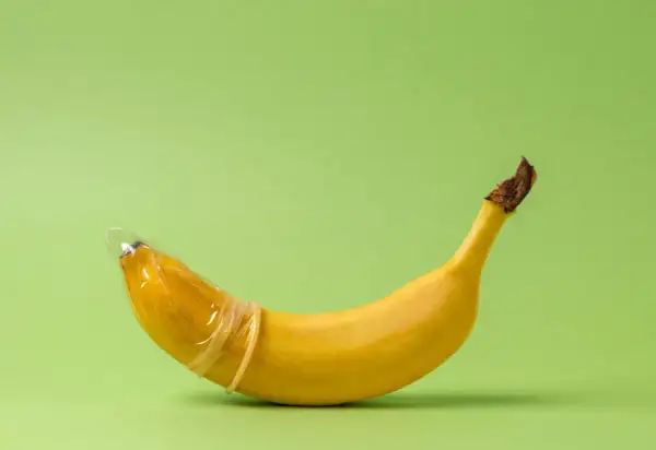 Banan w prezerwatywie, symbolizujący penis 23 cm, na zielonym tle.