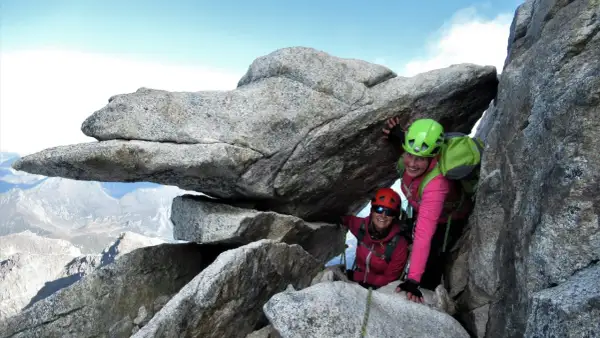 Zwei Bergsteigerinnen auf dem Olperer Nordgrat, lächelnd unter einem Felsvorsprung.