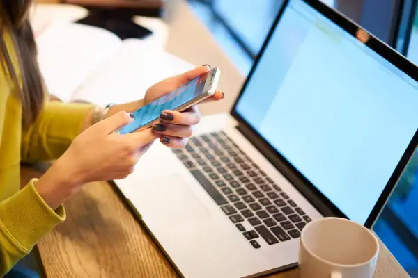 Kobieta pisze kod Swift na telefonie, obok leży laptop.